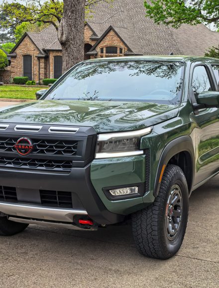 A Tactical Green 2026 Nissan Frontier Pro-4X parked on a rocky mountain outcrop overlooking a vast mountain range.